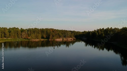 Aerial shot flying forward and up above still calm waters of northern lake with reflectioins revealing endless boreal pine trees coniferous forest going over horizon.  Grundy lake, Ontario, Canada. photo