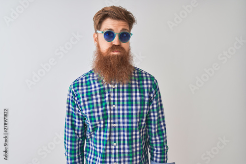 Young redhead irish man wearing casual shirt and sunglasses over isolated white background puffing cheeks with funny face. Mouth inflated with air, crazy expression.