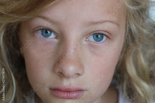 Closeup of a beautiful preteen girl with blue eyes and a sad, serious stare