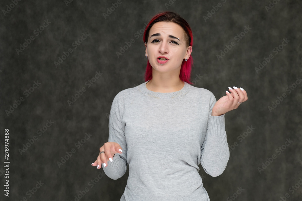 Portrait to the waist of a pretty girl with red hair on a gray background in a gray sweater. Standing right in front of the camera in a studio with emotions, talking, showing hands, smiling Portrait to the waist of a pretty girl with red hair on a gray background in a gray sweater. Standing right in front of the camera in a studio with emotions, talking, showing hands, smiling