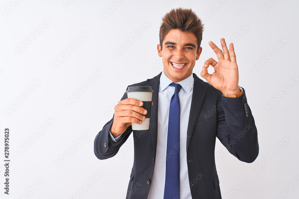 Young handsome businessman wearing suit holding coffee over isolated white background doing ok sign with fingers, excellent symbol Young handsome businessman wearing suit holding coffee over isolated white background doing ok sign with fingers, excellent symbol