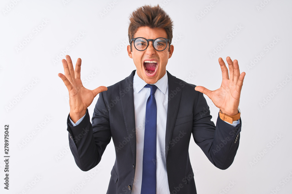 Young handsome businessman wearing suit and glasses over isolated white background crazy and mad shouting and yelling with aggressive expression and arms raised. Frustration concept. Young handsome businessman wearing suit and glasses over isolated white background crazy and mad shouting and yelling with aggressive expression and arms raised. Frustration concept.