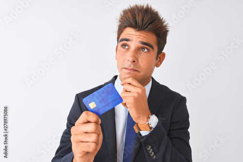 Young handsome businessman wearing suit holding credit card over isolated white background serious face thinking about question, very confused idea