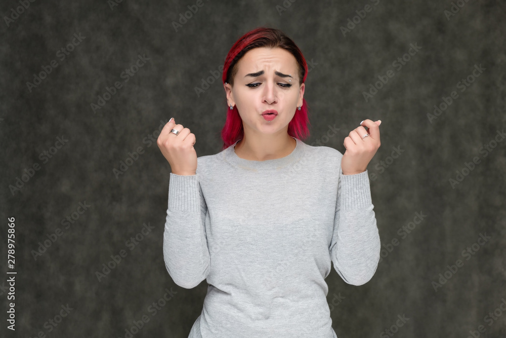 Portrait to the waist of a pretty girl with red hair on a gray background in a gray sweater. Standing right in front of the camera in a studio with emotions, talking, showing hands, smiling Portrait to the waist of a pretty girl with red hair on a gray background in a gray sweater. Standing right in front of the camera in a studio with emotions, talking, showing hands, smiling