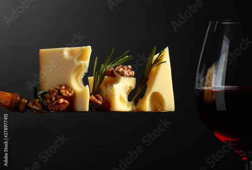 Cheese with walnuts, rosemary and red wine on a black background.