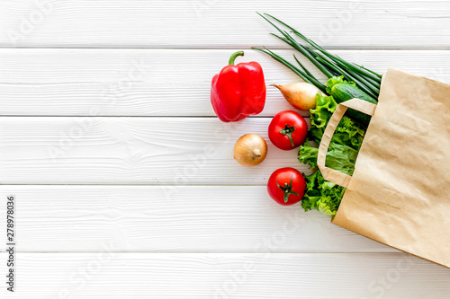 Buying fresh vegetables in paper bag on white wooden background top view copyspace