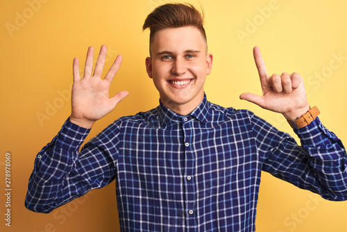 Young handsome man wearing casual shirt standing over isolated yellow background showing and pointing up with fingers number seven while smiling confident and happy.