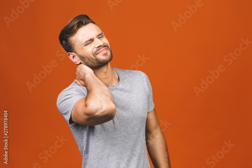Feeling pain in neck. Frustrated young man touching his neck and expressing negativity while standing against orange background