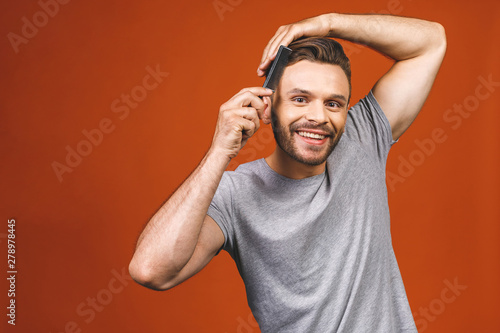 Portrait of handsome young man combing his hair in bathroom. Isolated over orange background.