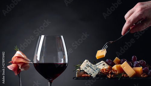 Glass of red wine with various cheeses , fruits and prosciutto on a black background.