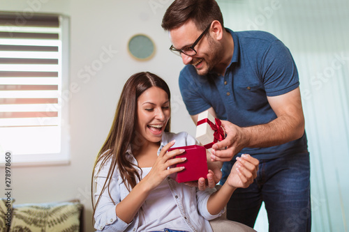 Smiling man surprises his girlfriend with present at home