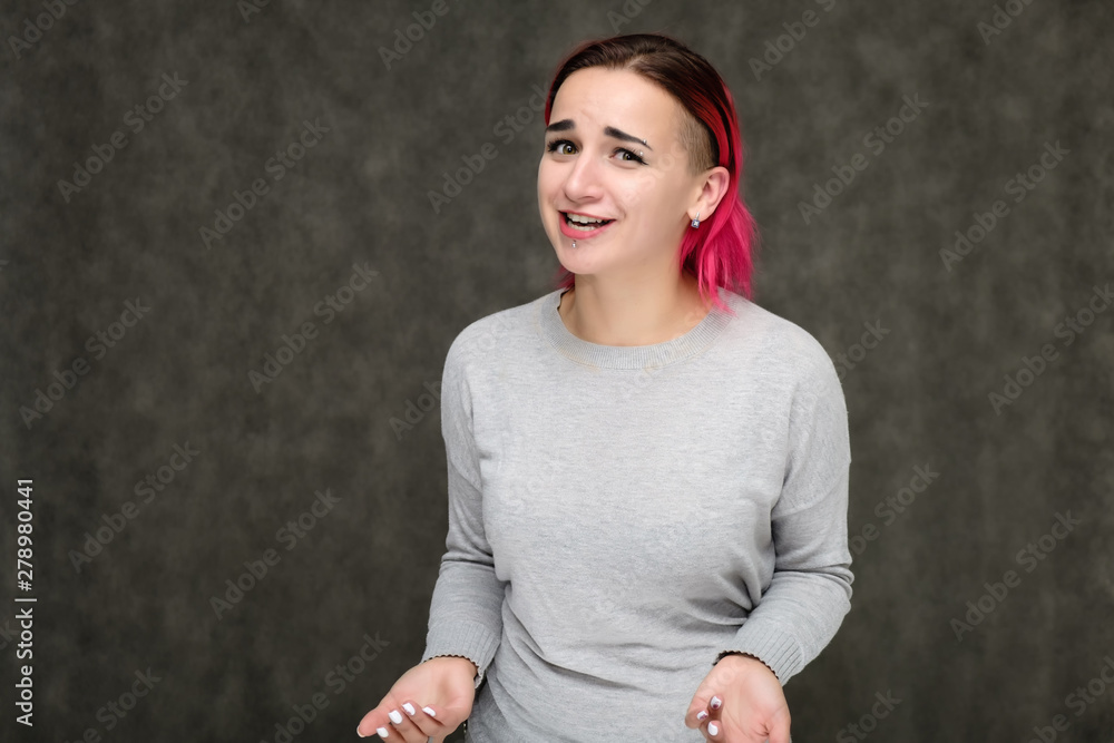 Portrait to the waist of a pretty girl with red hair on a gray background in a gray sweater. Standing right in front of the camera in a studio with emotions, talking, showing hands, smiling Portrait to the waist of a pretty girl with red hair on a gray background in a gray sweater. Standing right in front of the camera in a studio with emotions, talking, showing hands, smiling