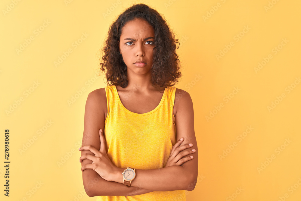 Young brazilian woman wearing t-shirt standing over isolated yellow background skeptic and nervous, disapproving expression on face with crossed arms. Negative person. Young brazilian woman wearing t-shirt standing over isolated yellow background skeptic and nervous, disapproving expression on face with crossed arms. Negative person.