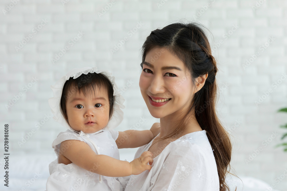 Happy Beauty mother Holding Cute Sweet Adorable Asian Baby wearing white dress sitting on Carpet smiling and playing with happiness emotional in cozy bedroom,Healthy Baby Concept Happy Beauty mother Holding Cute Sweet Adorable Asian Baby wearing white dress sitting on Carpet smiling and playing with happiness emotional in cozy bedroom,Healthy Baby Concept