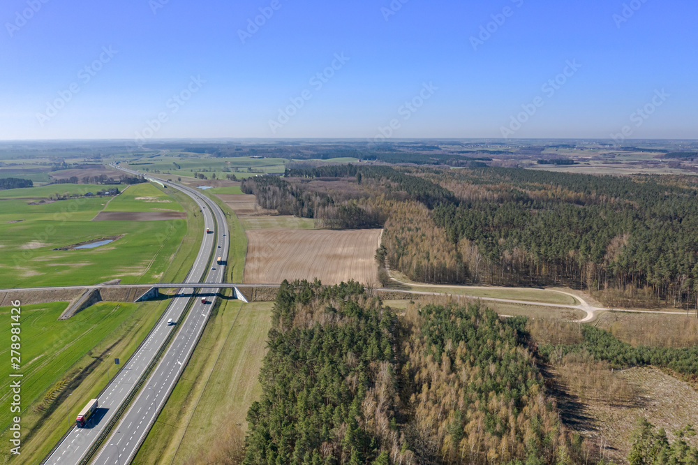 Aerial view of multi-lane highway with moving cars through countryside and forest in summer afternoon. Captured from above with a drone. Poland, A1, Europe. Aerial view of multi-lane highway with moving cars through countryside and forest in summer afternoon. Captured from above with a drone. Poland, A1, Europe.