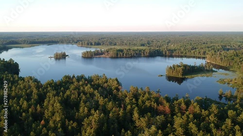 Aerial shot flying forward and down to boreal pine coniferous forest and northern lake. Overlooking beautiful landscape of northern boreal forest going over horizon.  Grundy lake, Ontario, Canada. photo