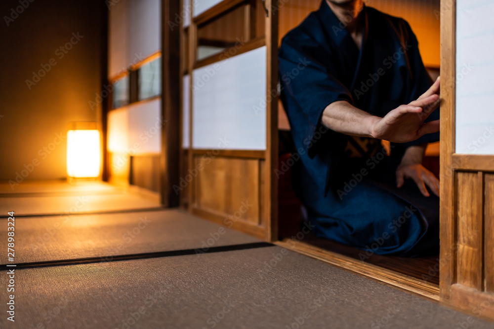 Fototapeta premium Traditional japanese house or ryokan with man in kimono opening shoji sliding doors sitting on tatami mat floor