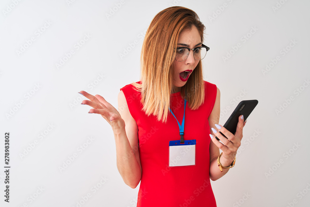 Naklejka premium Redhead businesswoman wearing id card using smartphone over isolated white background very happy and excited, winner expression celebrating victory screaming with big smile and raised hands