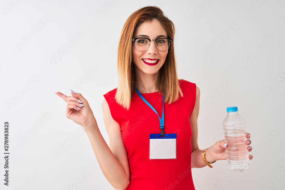 Redhead businesswoman wearing id card drinking water over isolated white background very happy pointing with hand and finger to the side Redhead businesswoman wearing id card drinking water over isolated white background very happy pointing with hand and finger to the side