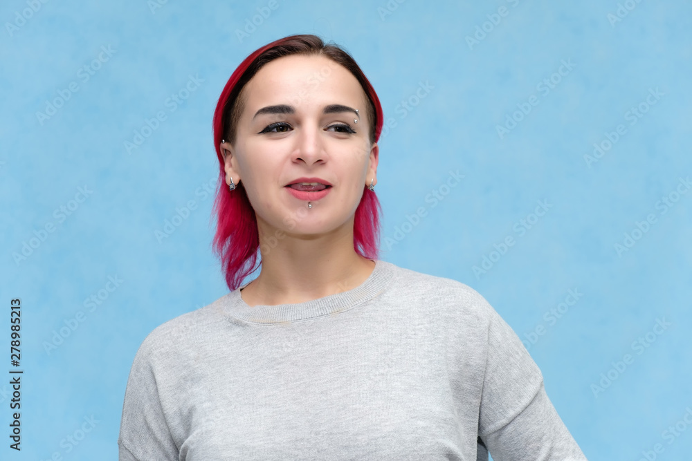 Portrait of the chest of a pretty girl with red hair on a blue background in a gray jacket. Standing in the studio right in front of the camera with emotions, talking, showing hands, smiling Portrait of the chest of a pretty girl with red hair on a blue background in a gray jacket. Standing in the studio right in front of the camera with emotions, talking, showing hands, smiling