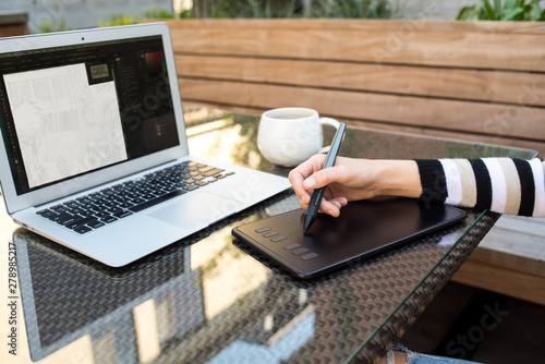 Detail photo of woman using drawing tablet and laptop on outdoor patio