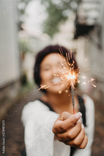 A beautiful young black woman holding up a sparkler in the summer