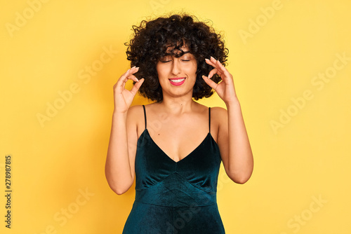 Young arab woman with curly hair wearing elegant dress over isolated yellow background relax and smiling with eyes closed doing meditation gesture with fingers. Yoga concept.