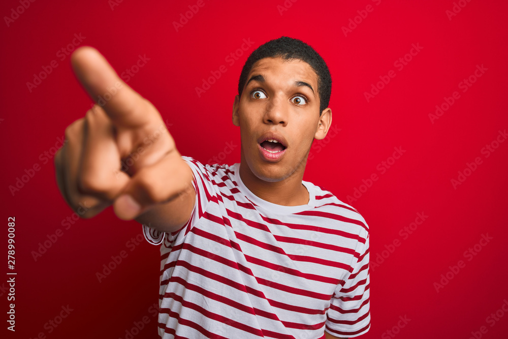 Fototapeta premium Young handsome arab man wearing striped t-shirt over isolated red background Pointing with finger surprised ahead, open mouth amazed expression, something on the front