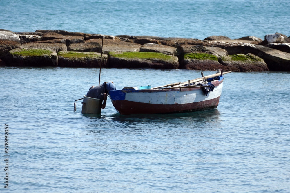 Pescatore sulla barca mentre perlustra il fondale del mare dentro uno scafandro artigianale. Sud Italia