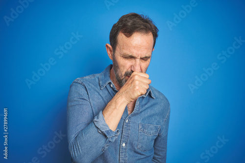 Handsome middle age senior man with grey hair over isolated blue background feeling unwell and coughing as symptom for cold or bronchitis. Healthcare concept.