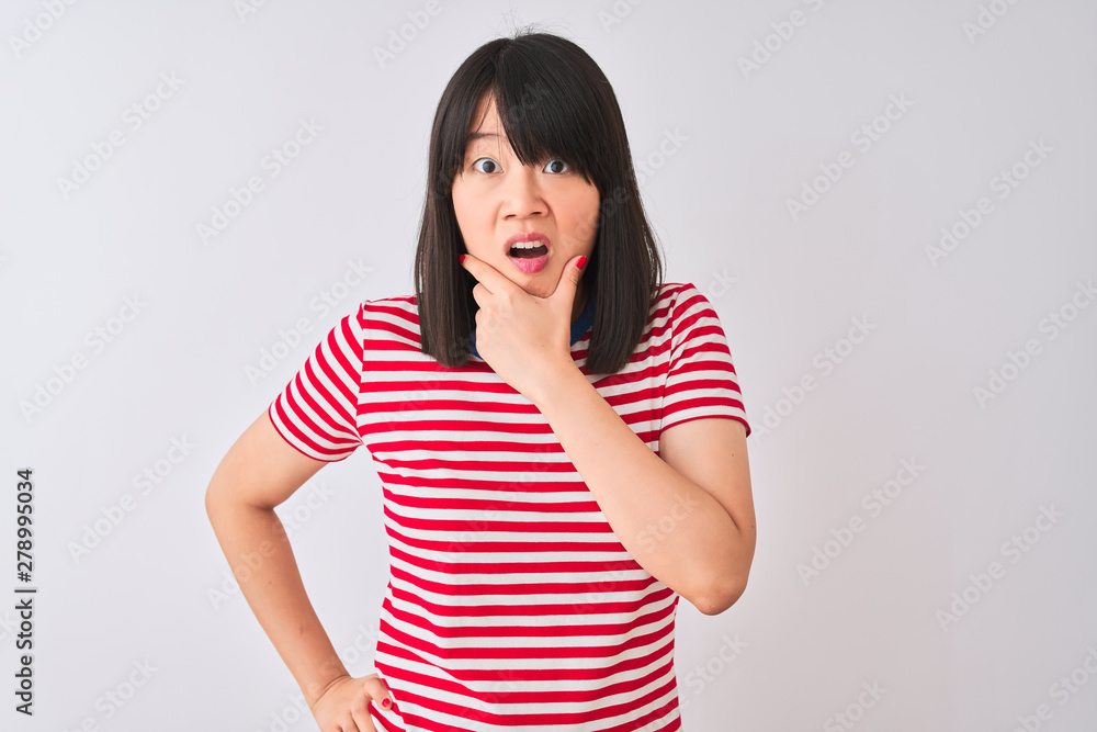 Young beautiful chinese woman wearing red striped t-shirt over isolated white background Looking fascinated with disbelief, surprise and amazed expression with hands on chin Young beautiful chinese woman wearing red striped t-shirt over isolated white background Looking fascinated with disbelief, surprise and amazed expression with hands on chin