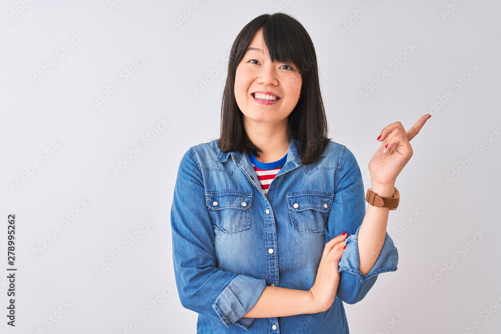 Young beautiful chinese woman wearing denim shirt over isolated white background with a big smile on face, pointing with hand and finger to the side looking at the camera. Young beautiful chinese woman wearing denim shirt over isolated white background with a big smile on face, pointing with hand and finger to the side looking at the camera.
