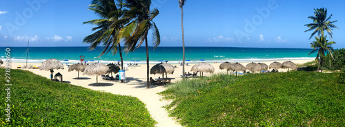 Panoramic view of tropical white sandy beach with blue sea, coconut palm tree, long chairs and umbrella. Tropical destination for relax holiday. Havana, CUBA. photo