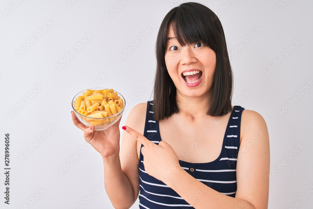 Young beautiful Chinese woman holding bowl with macaroni over isolated white background very happy pointing with hand and finger Young beautiful Chinese woman holding bowl with macaroni over isolated white background very happy pointing with hand and finger