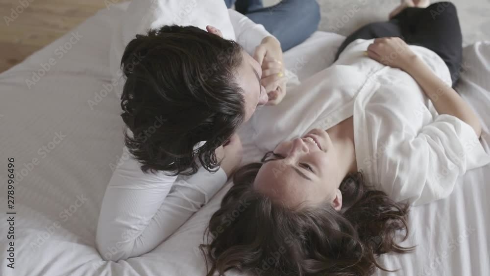 Overhead shot happy young couple lying on the bed talking close-up. Top view relaxing man and woman. Slow motion. Overhead shot happy young couple lying on the bed talking close-up. Top view relaxing man and woman. Slow motion.