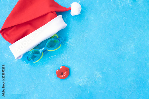 Hat of Santa Claus with goggles for swimming and a red lips. Christmas vacation, sandals and swimming glasses by water, slippers and pool goggles near swimming pool