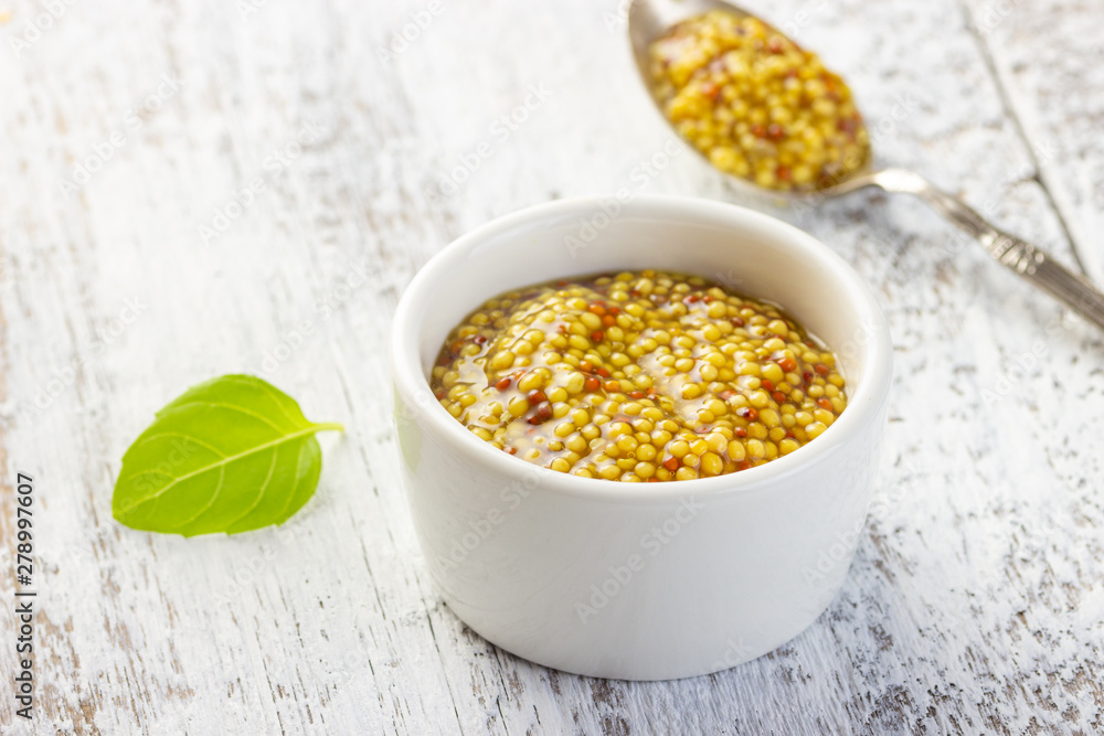 French grain mustard in a bowl on white wooden table. French grain mustard in a bowl on white wooden table.