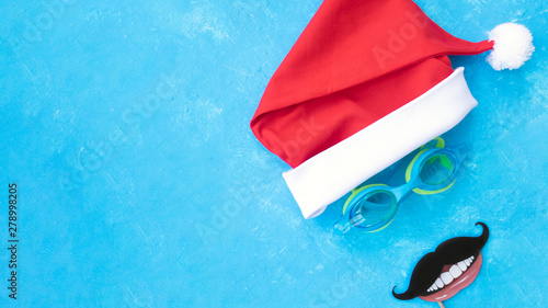 Banner. Hat of Santa Claus with goggles for swimming and the moustache and the smile. Christmas vacation, sandals and swimming glasses by water, slippers and pool goggles near swimming pool