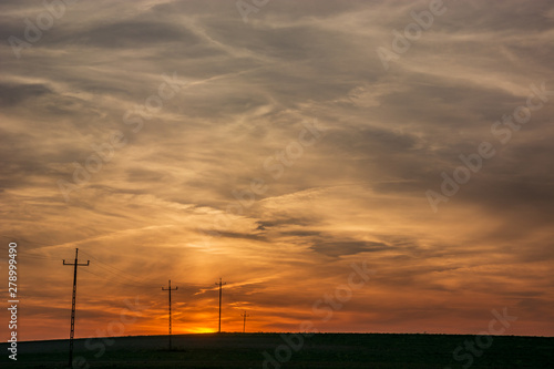 Electric poles in the field, sky and clouds after sunset