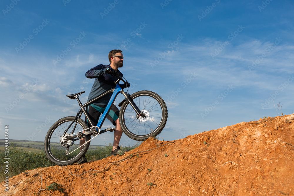 Cyclist in shorts and jersey on a modern carbon hardtail bike with an air suspension fork rides off-road on the orange-red hills at sunset evening in summer	