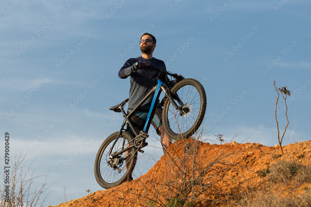 Fototapeta premium Cyclist in shorts and jersey on a modern carbon hardtail bike with an air suspension fork rides off-road on the orange-red hills at sunset evening in summer 