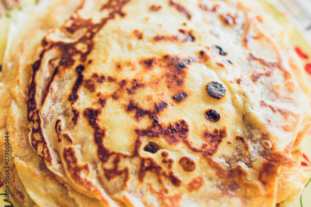 A stack of thin sweet pancakes on a plate - close-up top view - fatty in butter