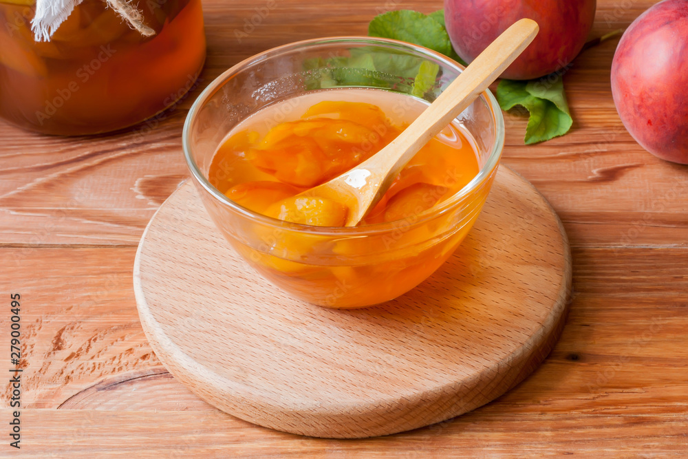 Piala with a spoon in homemade peach jam on a wooden round stand on the table in the morning sun. The concept of homemade conservation. Close up Piala with a spoon in homemade peach jam on a wooden round stand on the table in the morning sun. The concept of homemade conservation. Close up