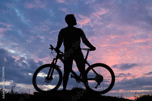 Cyclist in shorts and jersey on a modern carbon hardtail bike with an air suspension fork rides off-road on the orange-red hills at sunset evening in summer 