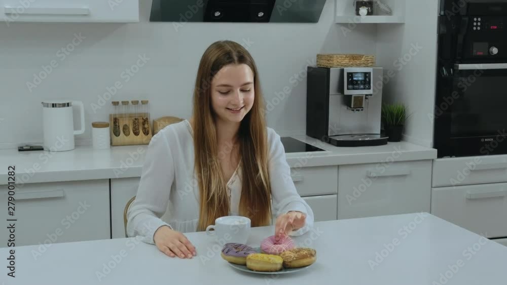 Young caucasian woman chooses donut, reviews and decides what to eat Young caucasian woman chooses donut, reviews and decides what to eat