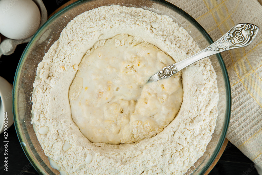 Making dough for pizza, flour with spoon in glass bowl on wooden cutting board, top view Making dough for pizza, flour with spoon in glass bowl on wooden cutting board, top view