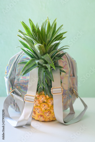 Pineapple with holographic bag on white wooden table over neo mint background. Tropical summer vacation, travel, back to school. Bag from material non-animal and non-environmentally harming benefits. photo