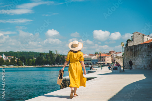 Obraz na plátně woman walking by sea quay in summer day in yellow sundress