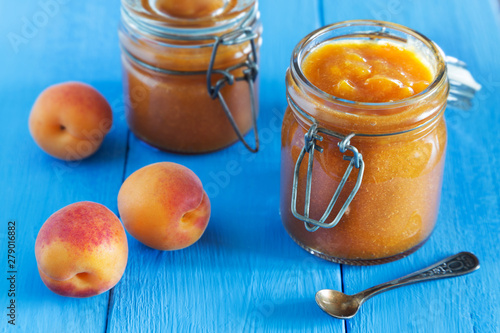 Jar of apricot jam with spoon and fruit on blue table