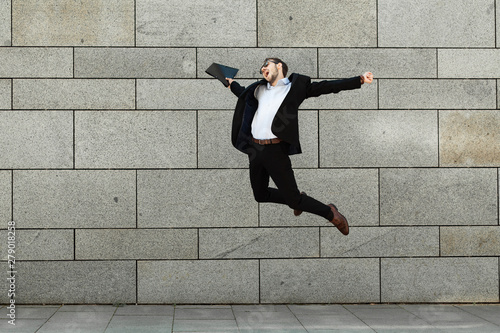 Young and cheerful businessman in suit jump on urban background. Success and victory, positive lifestyle. Award, reward.